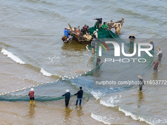 Fishermen cast long nets to catch seafood at the shore of the Yellow Sea in Lingshan Bay, West Coast New District, in Qingdao, China, on Oct...