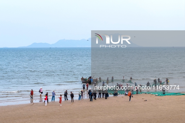 Fishermen cast long nets to catch seafood at the shore of the Yellow Sea in Lingshan Bay, West Coast New District, in Qingdao, China, on Oct...