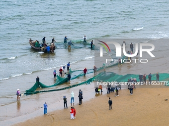 Fishermen cast long nets to catch seafood at the shore of the Yellow Sea in Lingshan Bay, West Coast New District, in Qingdao, China, on Oct...