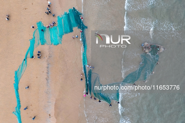 Fishermen cast long nets to catch seafood at the shore of the Yellow Sea in Lingshan Bay, West Coast New District, in Qingdao, China, on Oct...