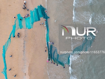 Fishermen cast long nets to catch seafood at the shore of the Yellow Sea in Lingshan Bay, West Coast New District, in Qingdao, China, on Oct...