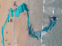 Fishermen cast long nets to catch seafood at the shore of the Yellow Sea in Lingshan Bay, West Coast New District, in Qingdao, China, on Oct...