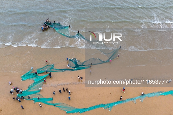 Fishermen cast long nets to catch seafood at the shore of the Yellow Sea in Lingshan Bay, West Coast New District, in Qingdao, China, on Oct...