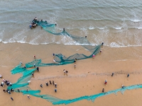 Fishermen cast long nets to catch seafood at the shore of the Yellow Sea in Lingshan Bay, West Coast New District, in Qingdao, China, on Oct...