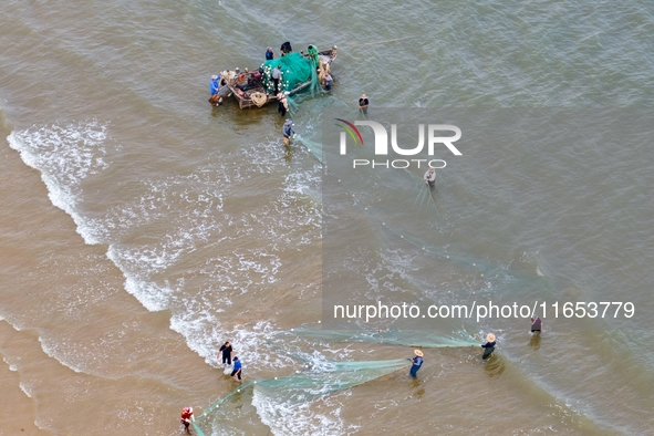 Fishermen cast long nets to catch seafood at the shore of the Yellow Sea in Lingshan Bay, West Coast New District, in Qingdao, China, on Oct...