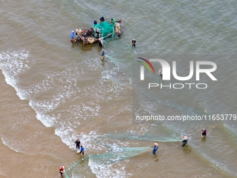 Fishermen cast long nets to catch seafood at the shore of the Yellow Sea in Lingshan Bay, West Coast New District, in Qingdao, China, on Oct...