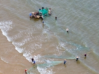 Fishermen cast long nets to catch seafood at the shore of the Yellow Sea in Lingshan Bay, West Coast New District, in Qingdao, China, on Oct...