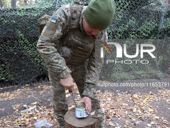 A soldier from the 2S1 Gvozdika self-propelled howitzer crew of Ukraine's 154th Separate Mechanized Brigade opens a tin can with a knife at...