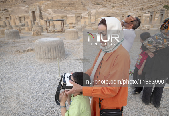 An Iranian woman helps her young son use VR glasses while visiting the Persepolis historical site near the city of Shiraz in Fars province,...