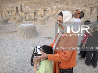 An Iranian woman helps her young son use VR glasses while visiting the Persepolis historical site near the city of Shiraz in Fars province,...