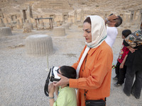 An Iranian woman helps her young son use VR glasses while visiting the Persepolis historical site near the city of Shiraz in Fars province,...