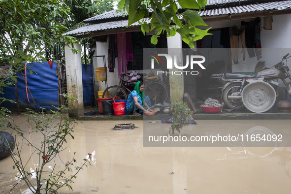 A woman washes essential items in floodwaters in front of her house in a village in Jhenaigati upazila of Sherpur district, Bangladesh, on O...