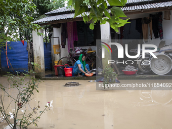 A woman washes essential items in floodwaters in front of her house in a village in Jhenaigati upazila of Sherpur district, Bangladesh, on O...