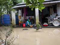 A woman washes essential items in floodwaters in front of her house in a village in Jhenaigati upazila of Sherpur district, Bangladesh, on O...