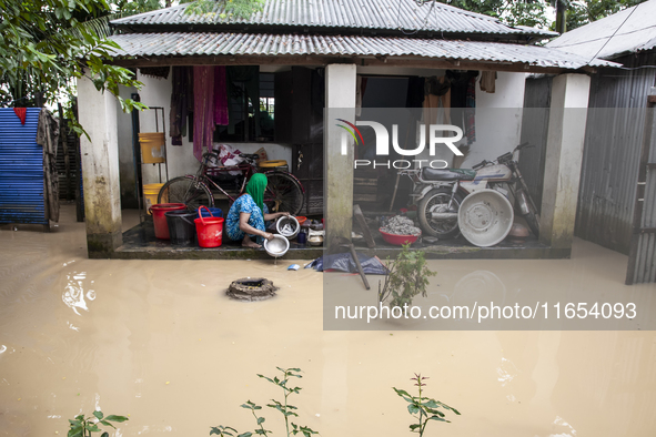 A woman washes essential items in floodwaters in front of her house in a village in Jhenaigati upazila of Sherpur district, Bangladesh, on O...