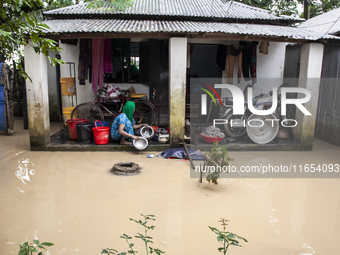 A woman washes essential items in floodwaters in front of her house in a village in Jhenaigati upazila of Sherpur district, Bangladesh, on O...