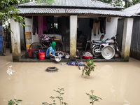 A woman washes essential items in floodwaters in front of her house in a village in Jhenaigati upazila of Sherpur district, Bangladesh, on O...