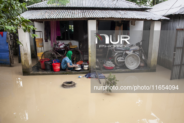 A woman washes essential items in floodwaters in front of her house in a village in Jhenaigati upazila of Sherpur district, Bangladesh, on O...