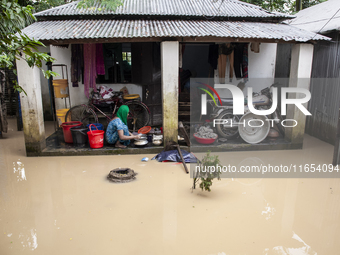 A woman washes essential items in floodwaters in front of her house in a village in Jhenaigati upazila of Sherpur district, Bangladesh, on O...