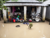 A woman washes essential items in floodwaters in front of her house in a village in Jhenaigati upazila of Sherpur district, Bangladesh, on O...