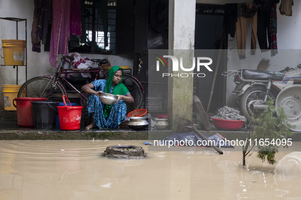 A woman washes essential items in floodwaters in front of her house in a village in Jhenaigati upazila of Sherpur district, Bangladesh, on O...