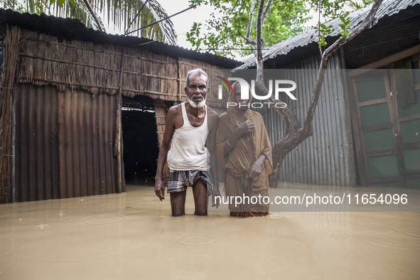 An elderly husband and wife stand in front of their house in knee-deep flood water in a village in Jhenaigati upazila of Sherpur district in...