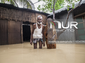 An elderly husband and wife stand in front of their house in knee-deep flood water in a village in Jhenaigati upazila of Sherpur district in...