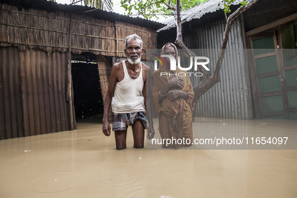 An elderly husband and wife stand in front of their house in knee-deep flood water in a village in Jhenaigati upazila of Sherpur district in...