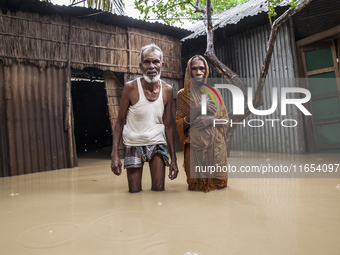 An elderly husband and wife stand in front of their house in knee-deep flood water in a village in Jhenaigati upazila of Sherpur district in...