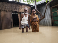 An elderly husband and wife stand in front of their house in knee-deep flood water in a village in Jhenaigati upazila of Sherpur district in...