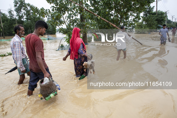 People walk through knee-deep flooded streets carrying essentials in a village in Jhenaigati upazila of Sherpur district in Sherpur, Banglad...