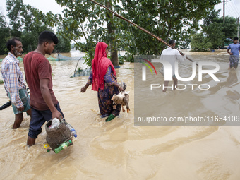 People walk through knee-deep flooded streets carrying essentials in a village in Jhenaigati upazila of Sherpur district in Sherpur, Banglad...