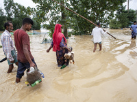 People walk through knee-deep flooded streets carrying essentials in a village in Jhenaigati upazila of Sherpur district in Sherpur, Banglad...