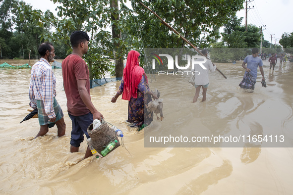 People walk through knee-deep flooded streets carrying essentials in a village in Jhenaigati upazila of Sherpur district in Sherpur, Banglad...