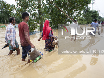 People walk through knee-deep flooded streets carrying essentials in a village in Jhenaigati upazila of Sherpur district in Sherpur, Banglad...