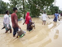 People walk through knee-deep flooded streets carrying essentials in a village in Jhenaigati upazila of Sherpur district in Sherpur, Banglad...