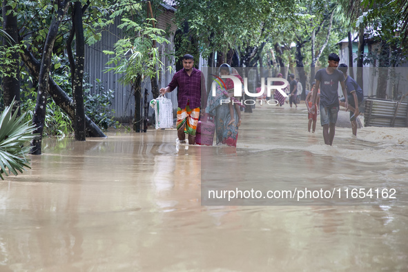 People walk through knee-deep flooded streets carrying essentials in a village in Jhenaigati upazila of Sherpur district in Sherpur, Banglad...