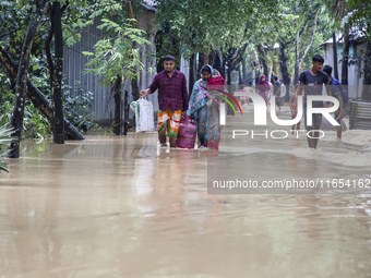 People walk through knee-deep flooded streets carrying essentials in a village in Jhenaigati upazila of Sherpur district in Sherpur, Banglad...