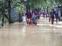 People walk through knee-deep flooded streets carrying essentials in a village in Jhenaigati upazila of Sherpur district in Sherpur, Banglad...