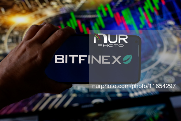 In this photo illustration, the Bitfinex logo is seen displayed on a smartphone screen against a computer screen displaying a stock market g...