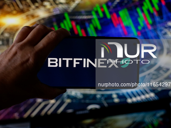 In this photo illustration, the Bitfinex logo is seen displayed on a smartphone screen against a computer screen displaying a stock market g...