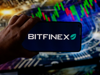 In this photo illustration, the Bitfinex logo is seen displayed on a smartphone screen against a computer screen displaying a stock market g...