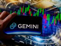 In this photo illustration, the Gemini logo is seen displayed on a smartphone screen against a computer screen displaying a stock market gra...