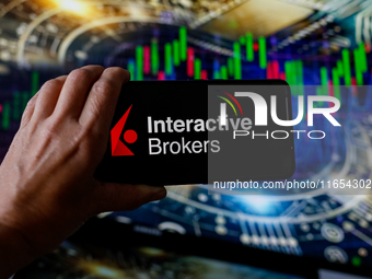 In this photo illustration, the Interactive Brokers logo is seen displayed on a smartphone screen against a computer screen displaying a sto...