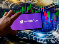 In this photo illustration, the Wealthfront logo is seen displayed on a smartphone screen against a computer screen displaying a stock marke...