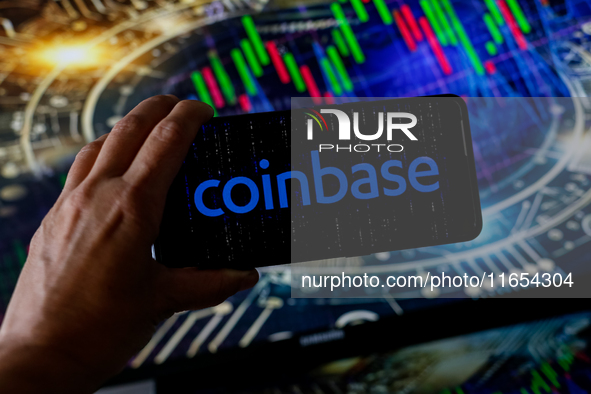 In this photo illustration, the Coinbase logo is seen displayed on a smartphone screen against a computer screen displaying a stock market g...