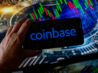 In this photo illustration, the Coinbase logo is seen displayed on a smartphone screen against a computer screen displaying a stock market g...