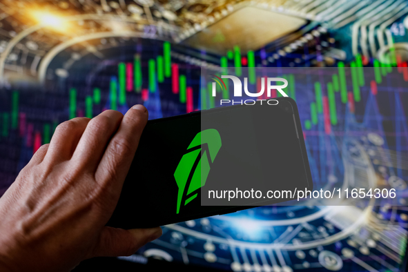 In this photo illustration, the Robinhood logo is seen displayed on a smartphone screen against a computer screen displaying a stock market...