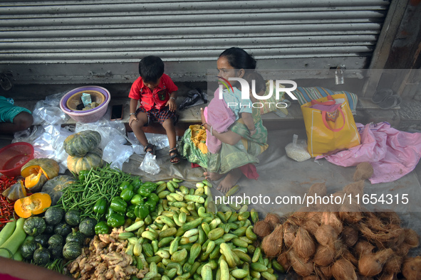 A woman holds her baby in her arms while selling vegetables inside a market in Kolkata, India, on October 10, 2024. 