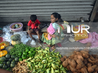 A woman holds her baby in her arms while selling vegetables inside a market in Kolkata, India, on October 10, 2024. (